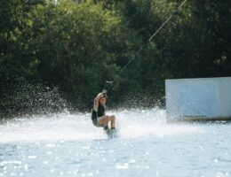Kind fährt beim Wakeboarden an einer Rampe über einen Binnensee