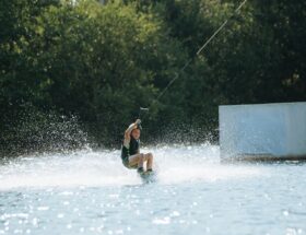 Kind fährt beim Wakeboarden an einer Rampe über einen Binnensee