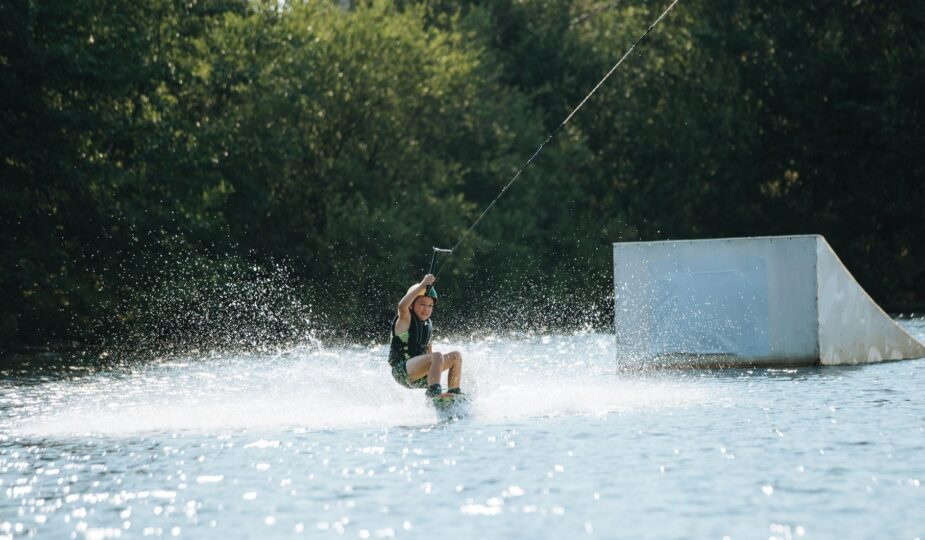 Kind fährt beim Wakeboarden an einer Rampe über einen Binnensee