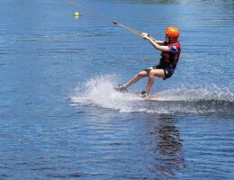Wasserskifahrer mit Helm gleitet an einem Seil über den See