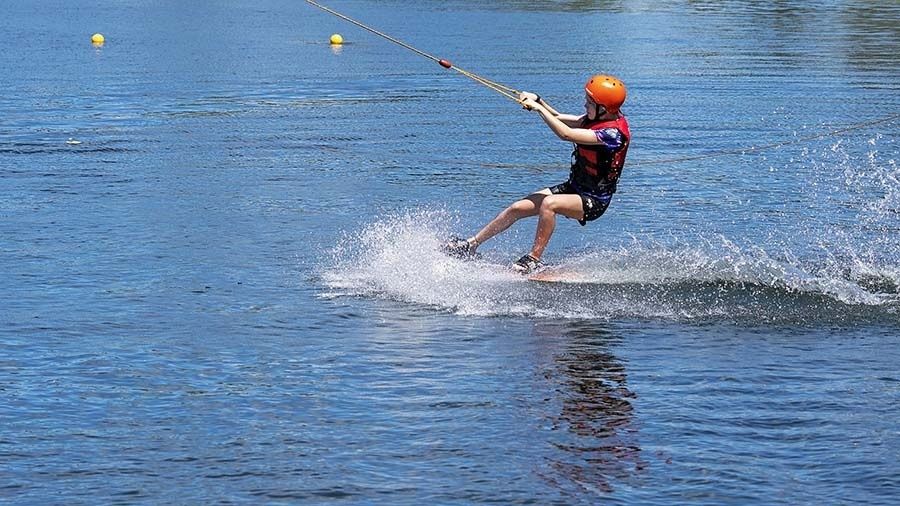 Wasserskifahrer mit Helm gleitet an einem Seil über den See